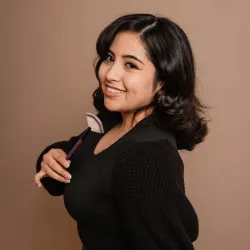 Alejandra smiling and  holding a purple facial brush